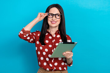 Wall Mural - Portrait of good mood smart girl wear red shirt touch eyewear hold tablet look at promo empty space isolated on blue color background