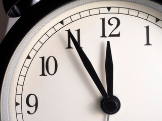 The dial of a clock, the hands of which show the time at five minutes to twelve. Close up.
