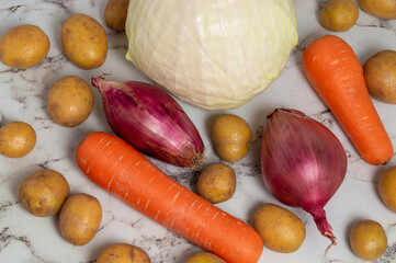 A variety of vegetables including potatoes, onions, and carrots are displayed on a counter. Concept of abundance and freshness, as the vegetables are piled up in a visually appealing manner