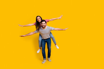 Poster - Full length photo of carefree couple boyfriend holding on back pretty girl hold arms like wings isolated on vivid yellow color background