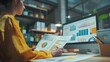 © yj - Paper with charts and graphs around on the desk in a modern office environment. An IT project manager is at a desk, working at a computer. generative AI