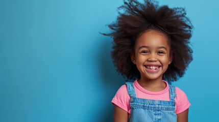 Wall Mural - young African American girl with a big smile, wearing a pink shirt and a blue denim jumper, set against a light blue background