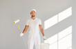 © Studio Romantic - Portrait of a happy smiling male painter in white clothes holding a bucket and paint roller standing in empty room on grey wall background. Renovation, apartment repair and renovating house concept.