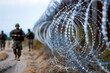 Uniformed border guards patrol along the barbed wire fence, tracking illegal border crossings by immigrants