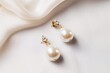 A pair of elegant pearl earrings, their lustrous sheen catching the light against the clean white canvas