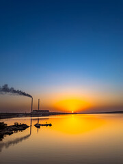 Wall Mural - The sun sets over lake with power plant emitting smoke in the background.