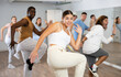 © JackF - Group of cheerful young adult diverse dancers performing dynamic movements with knee up in modern fitness studio