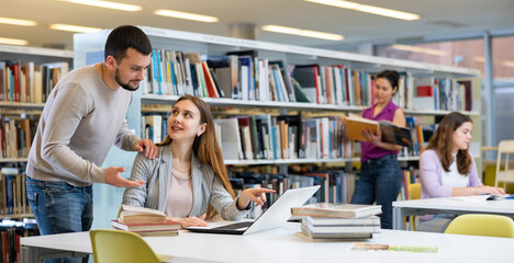 Canvas Print - Young guy and a girl students studying at the university, preparing for the exam in the library studying on a laptop ..and discussing something