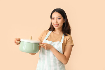 Poster - Happy beautiful Asian woman with cooking pot on beige background