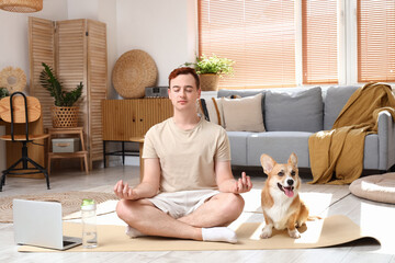 Sticker - Sporty young redhead man with cute Corgi dog meditating on yoga mat at home