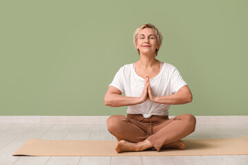 Sticker - Portrait of meditating mature woman sitting against green wall