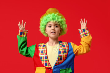 Poster - Surprised little boy in clown costume with raised hands on red background. April Fools Day celebration