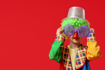 Poster - Cute little boy in clown costume with funny glasses and hat on red background. April Fools Day celebration