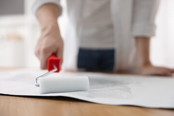 Sticker - Man applying glue onto wallpaper sheet at table indoors, closeup