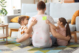Fototapeta Dmuchawce - Little children sticking KICK ME stickers to their father's back at home. April Fool's Day prank