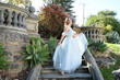 full length portrait of beautiful female model wearing blue fantasy ballgown, like a fairytale elf princess. Holding. Sword skirt, standing on staircase, walking up stairs of a romantic castle balcony