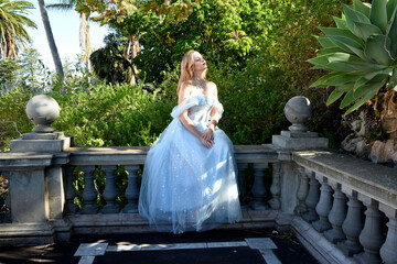 Poster - full length portrait of beautiful female model wearing blue fantasy ballgown, like a fairytale princess.  Sitting on staircase of  a romantic castle balcony location.