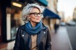 Portrait of a beautiful middle-aged woman with gray hair wearing glasses and a blue scarf in the city