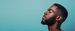 A serene black afro americanman in a tranquil state with eyes closed against a minimalist blue backdrop. Banner, copy space. Men's facial care concept, meditation.