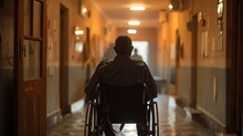 Solitary man in wheelchair facing the end of a dimly lit corridor, representing loneliness and accessibility issues.
