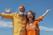 A couple smiling and celebrating with their arms outstretched against the blue sky