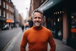 Portrait of a handsome middle-aged man in an orange sweater smiling at the camera on a city street.