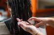Expert hairdresser applies revitalizing oil drops to woman's long black hair, transforming her look with a new hairstyle