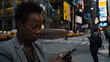 A focused individual looking at a smartphone in a vibrant city setting with illuminated advertisements and passing taxis