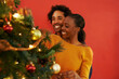 © Katie/peopleimages.com - Couple, Christmas and tree decoration in home with happiness for vacation celebration, giving or bonding. Man, woman and smile with lighting for winter season for family event, embrace or lounge