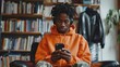 © Georgii - Close-up portrait of an African American teenage boy sitting indoors with headphones on, looking at a cell phone. Cool Zoomer with dreadlocks in a hoodie listens to a music mix or podcast online.