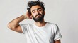 Handsome Arabian gentleman with bashful expression, curly bearded man wearing white casual tee standing alone on a white backdrop.