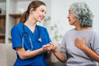 © NanSan - Caucasian female doctor offers encouragement to Asian mature elderly patient woman while holding hands, providing comfort and support during a medical consultation at sofa.