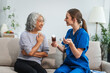 © NanSan - Caucasian female doctor introduces medicine to an elderly Asian patient while seated on a sofa, providing guidance and information about the prescribed medication.