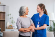 © NanSan - Caucasian female doctor assists in supporting an elderly Asian patient while they both sit on the sofa, ensuring comfort and stability during the interaction.