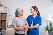 © NanSan - Caucasian female doctor assists in supporting an elderly Asian patient while they both sit on the sofa, ensuring comfort and stability during the interaction.