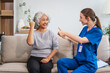 Caucasian female doctor shares a celebratory high five with an elderly Asian patient while both are seated together on the sofa.