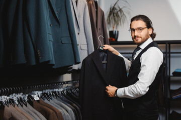 Wall Mural - Portrait business gentleman in glasses chooses to buy suit jacket in shop store classic clothes for men