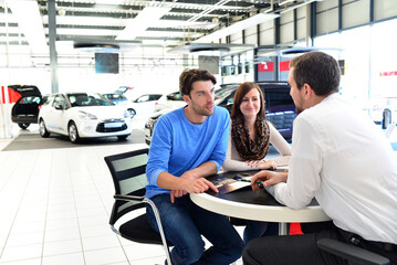 young couple buying a new car in the showroom of a car dealership - signature sales contract with seller