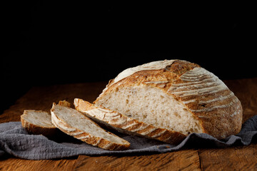 Fototapete - Rustic sourdough bread with cut slices on a wooden table. Panorama, black background with free space for text.	
