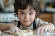 A small boy with dark hair and almond-shaped eyes carefully shaping dough into perfect circles with his tiny hands