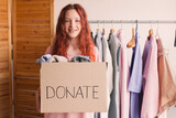 Fototapeta Zwierzęta - Smiling young woman putting clothing into donation box