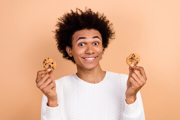 Canvas Print - Photo of cheerful funky man wear stylish clothes hand showing two tasty cookies break snack isolated on beige color background