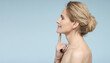 © Peakstock - Mature woman pointing finger at toned skin on her chin, thanks to anti-aging cosmetics and face contouring with beauty injections, side view on blue background