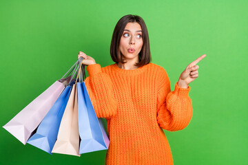 Wall Mural - Portrait of nice impressed lady hold store bags look direct finger empty space isolated on green color background