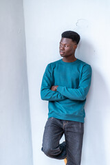 A young man in a blue sweatshirt and jeans stands against a white wall