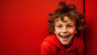 Kid with a Playful Expression Amidst the Solid Red Wall Background.