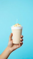 Wall Mural - A hand holding takeaway plastic cup of delicious white mocha on pastel blue background