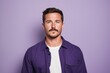 Portrait of a handsome young man with beard and mustache standing against purple background.