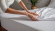 Woman's hands putting white fitted sheet on mattress