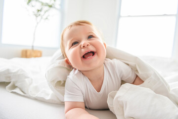 baby boy in white sunny bedroom. one years child relaxing in bed.
